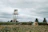 Rustic farm landscape with a large green water storage tank under a clear sky.
