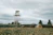 Rustic farm landscape with a large green water storage tank under a clear sky.