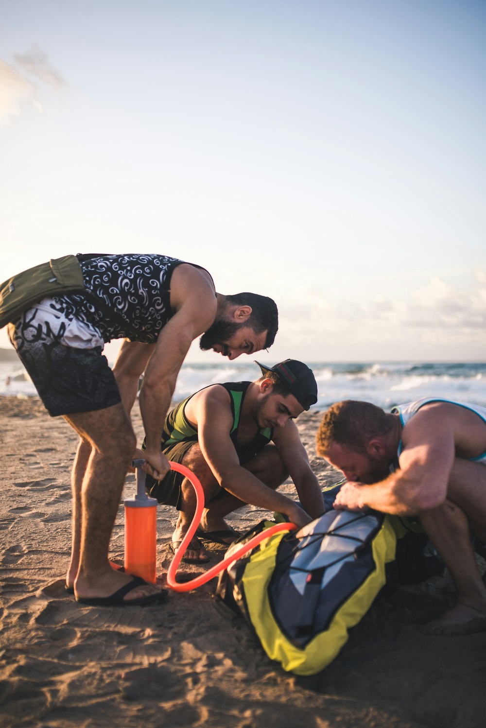 three men blowing air on bag in seashore