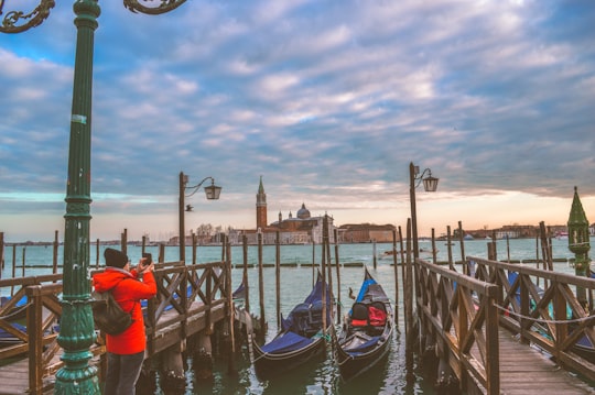 man using smartphone standing near two boats in Church of San Giorgio Maggiore Italy