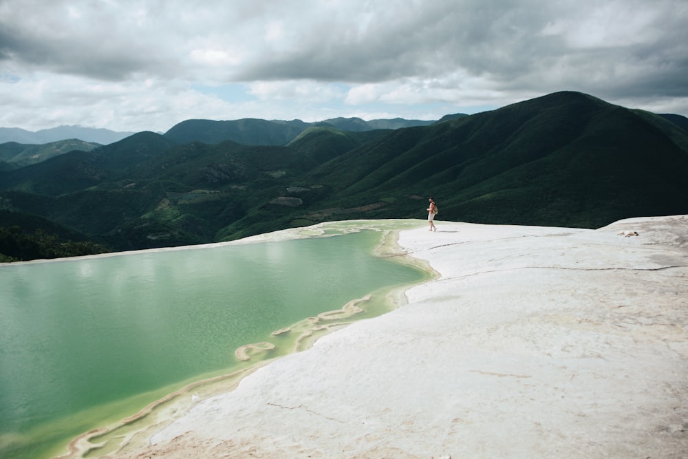 person standing infront of body of water with background of mountain