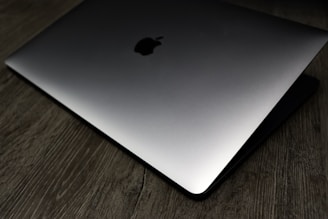 A sleek, partially closed laptop with a metallic finish is placed on a textured wooden surface. The lighting creates a gradient effect across the laptop, emphasizing its elegant design.