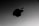 A close-up view of a metallic surface with a prominent black apple logo. The surface has a sleek and smooth texture with a subtle gradient of gray.