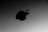 A close-up view of a metallic surface with a prominent black apple logo. The surface has a sleek and smooth texture with a subtle gradient of gray.
