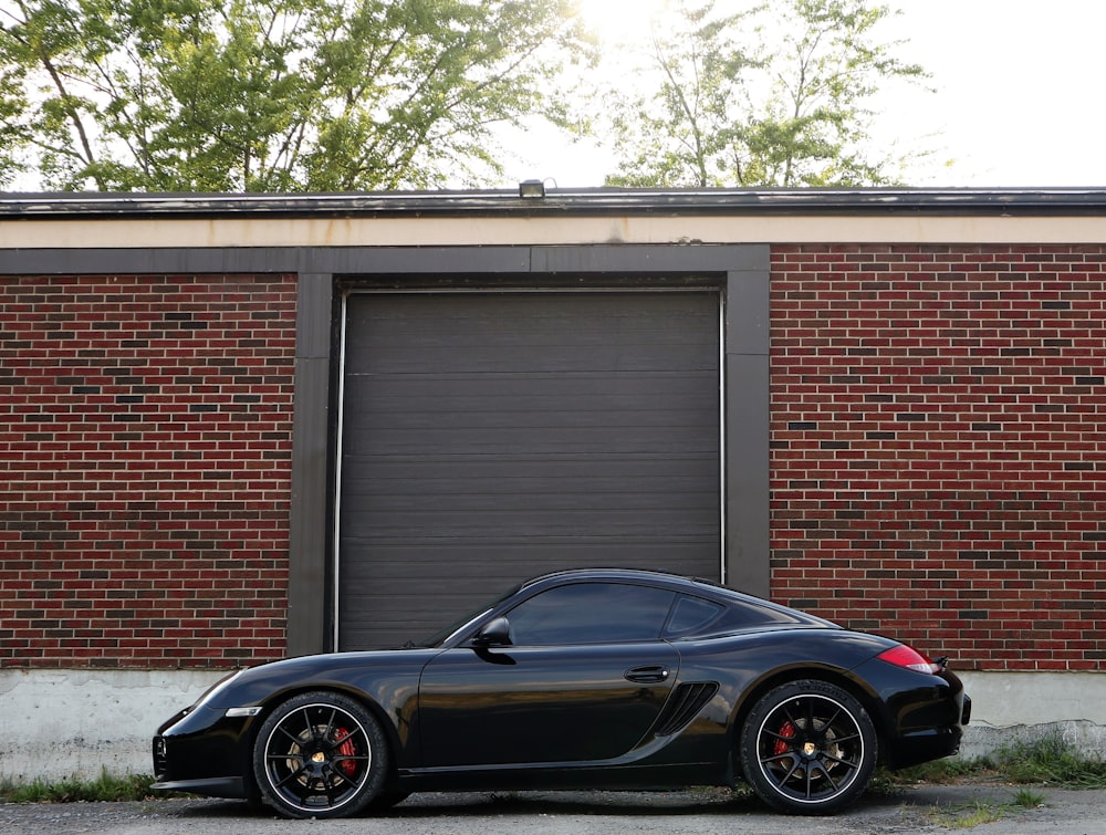 black Porsche 911 Carrera coupe parked beside brick wall