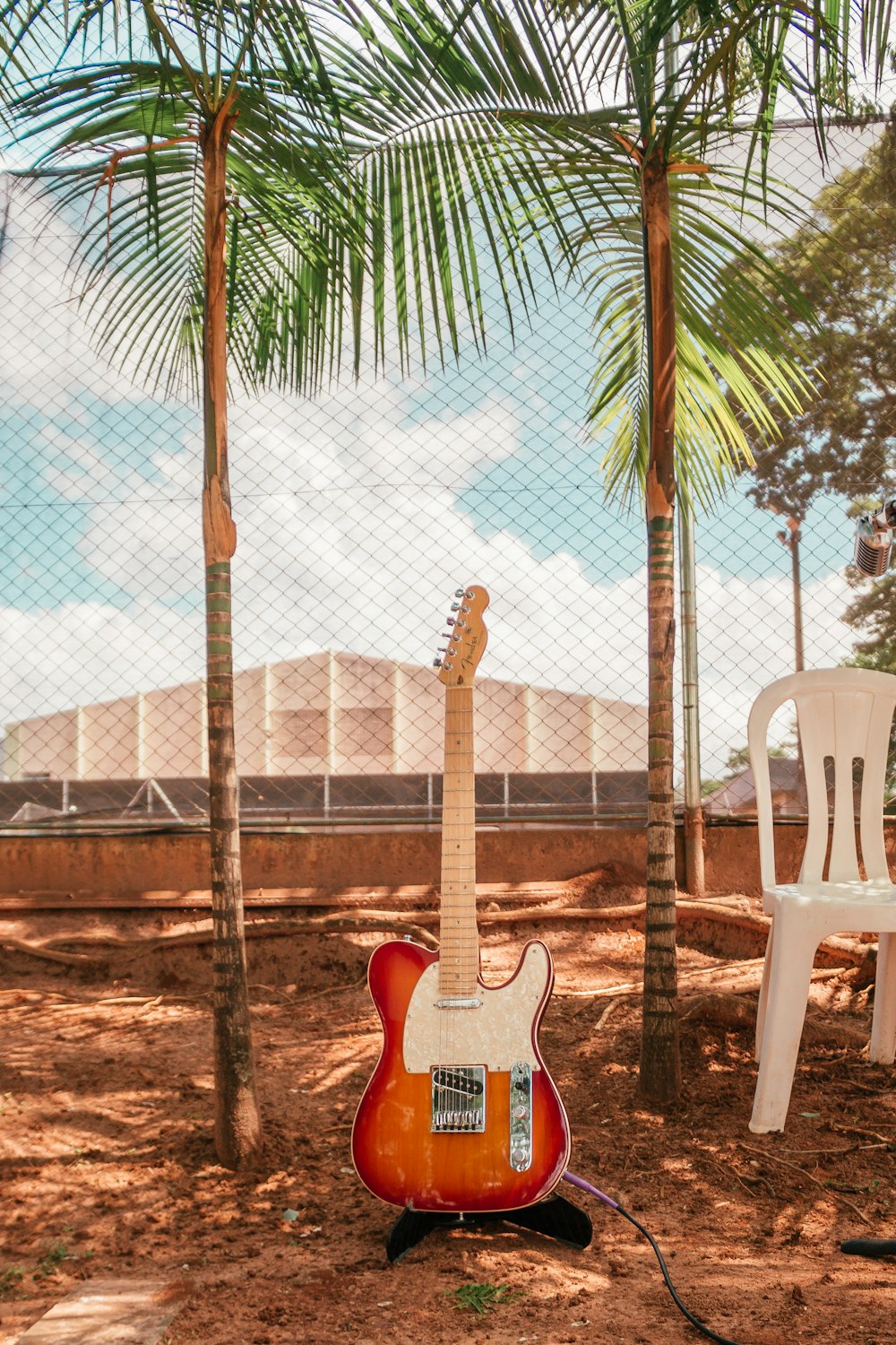 guitarra elétrica marrom e branca perto da cadeira monobloco e árvores durante o dia