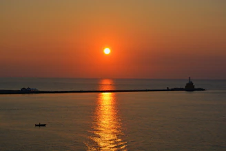 A vibrant sunset over a secluded Philippine island beach with a small fishing boat anchored near the shore.