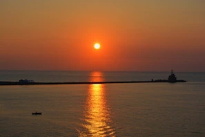 A vibrant sunrise over a tranquil bay with a small boat heading towards a lush island