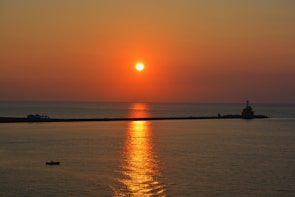 A vibrant sunset over a calm sea with a small sailboat on the horizon.