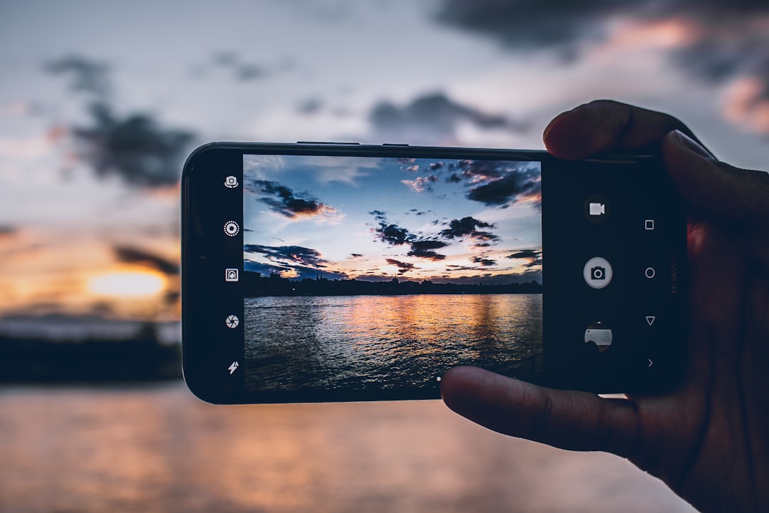 person filming body of water under blue sky