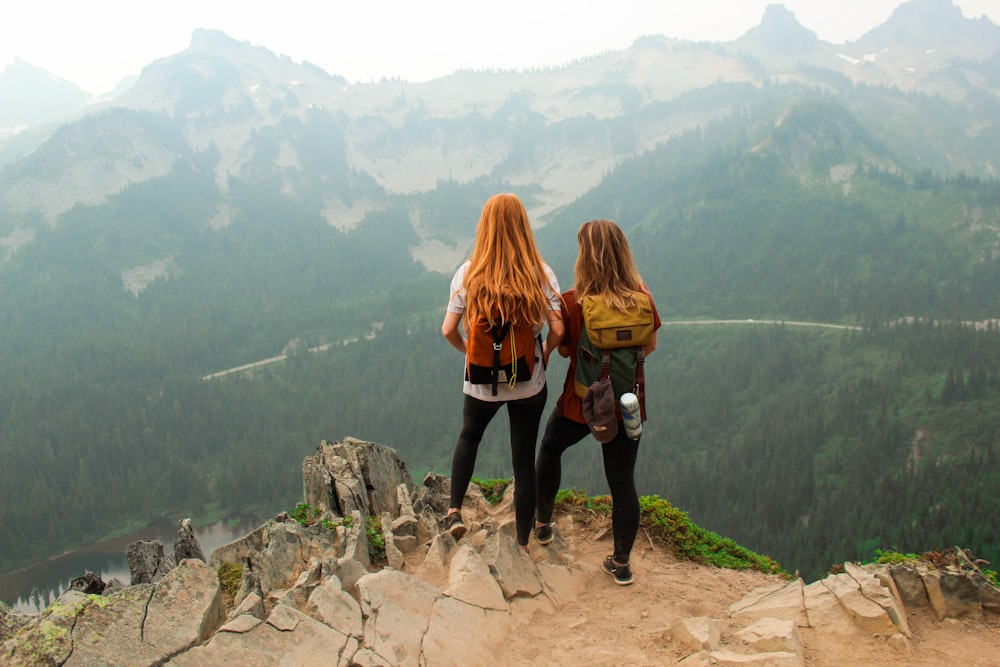 two women standing on cliff overlooking forest