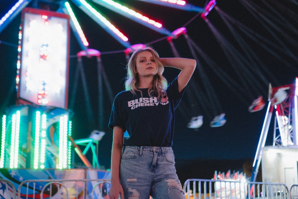 standing woman wearing black t-shirt and distressed blue denim bottoms with left hand on back of head post