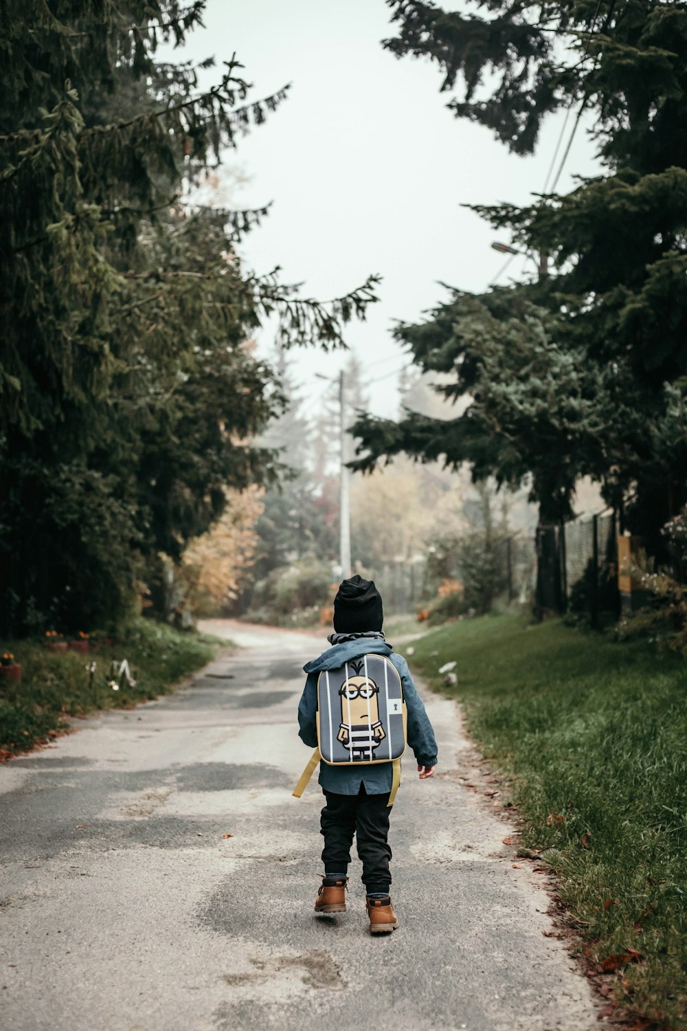 child carrying backpack while standing near green trees and plants