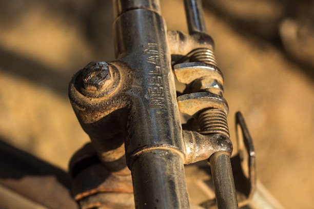 Close-up view of a metal clamp assembly, featuring bolts and screws with a slightly rusted and weathered appearance. The components are tightly connected, with intricate details visible on the metallic surfaces. The word 'IRELAND' is embossed on one of the metal parts. The background is blurred and indistinct, emphasizing the focus on the mechanical elements.
