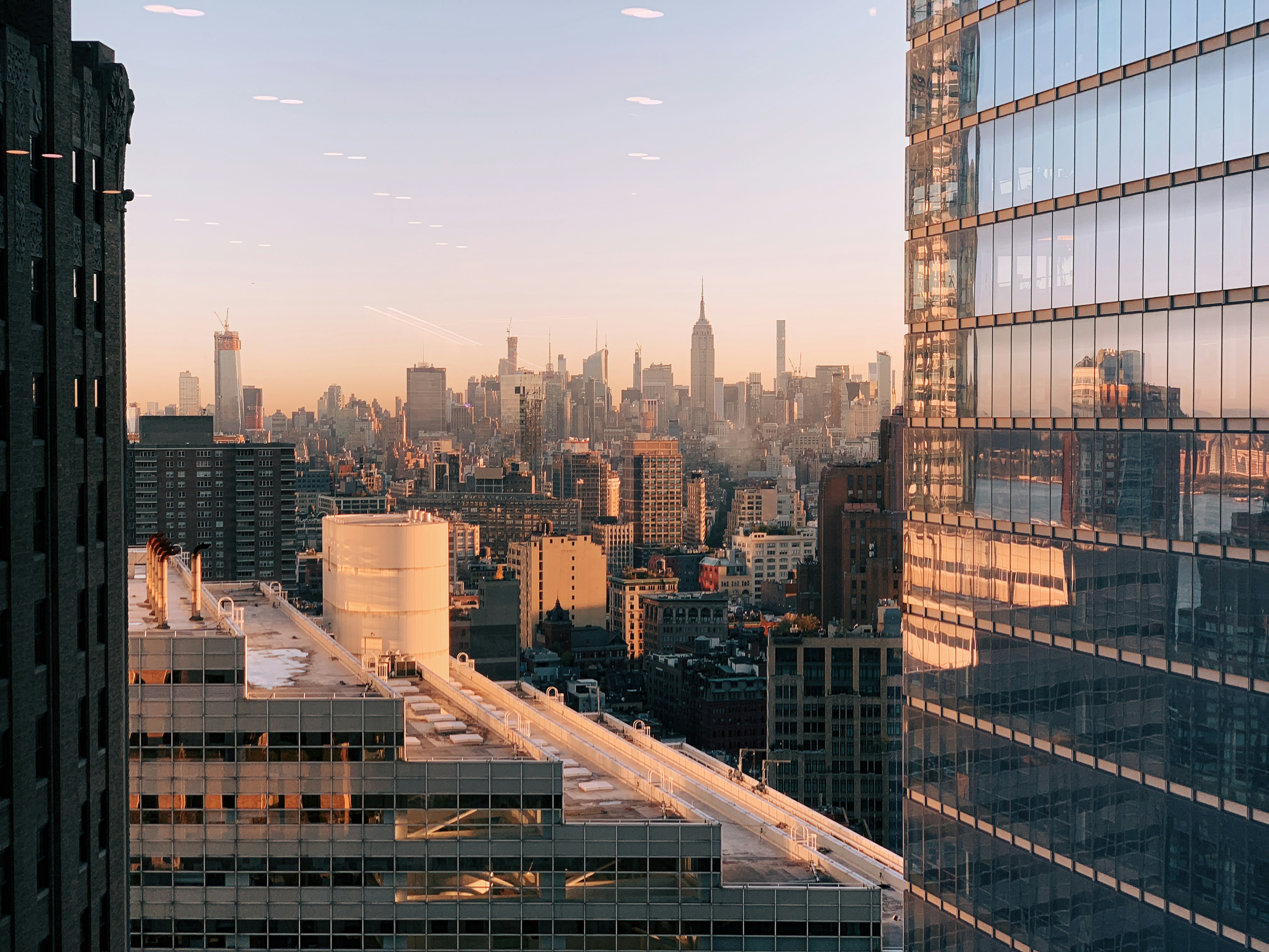 Modern glass-facade luxury penthouse exterior, Manhattan skyline at dusk, golden hour lighting, reflective windows