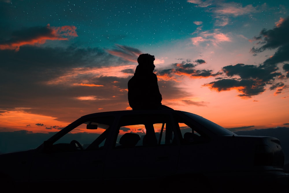 silhouette of man sitting on car roof