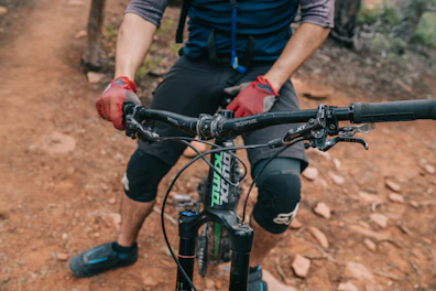 Wrist guards worn by a cyclist gripping handlebars on a mountain trail