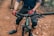 A cyclist wearing gloves and knee pads is gripping the handlebars of a mountain bike. The bike is on a rugged dirt trail, and the cyclist's lower half is visible.