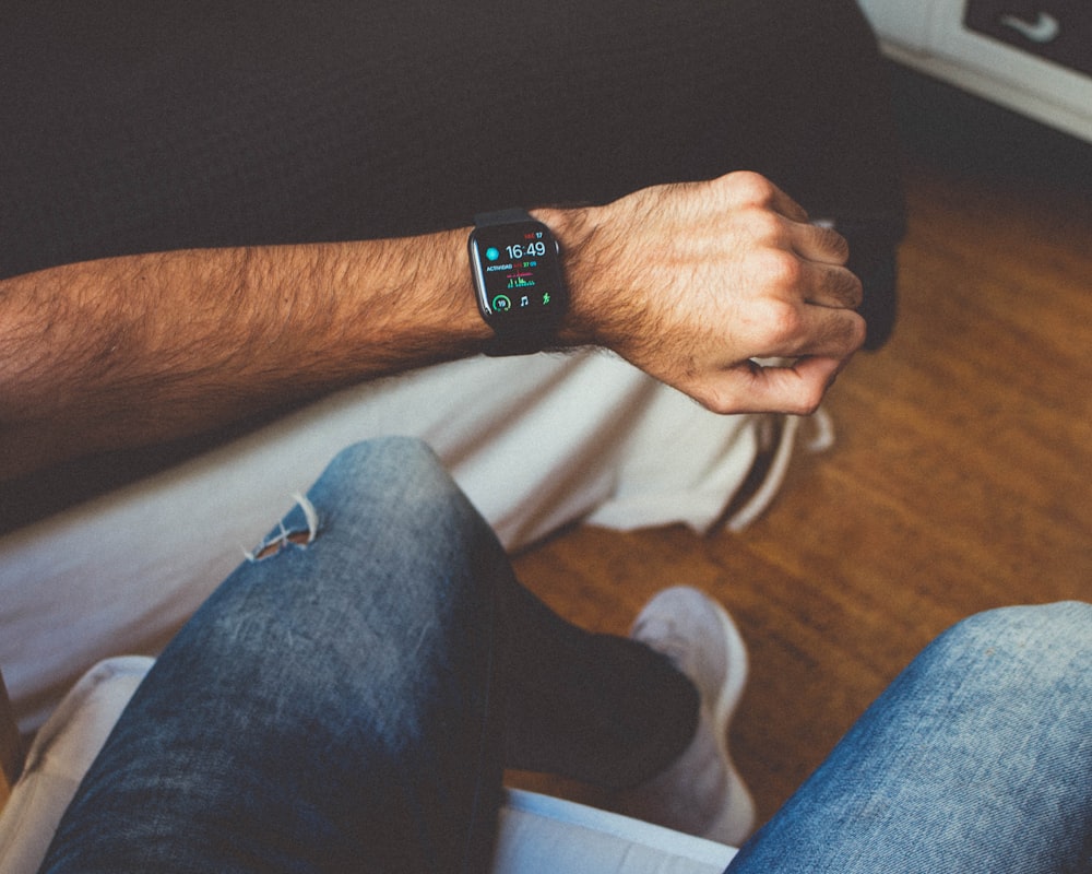 sitting man in blue denim jeans showing smartwatch