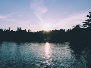 A peaceful lake reflecting the surrounding trees and sky at sunset.