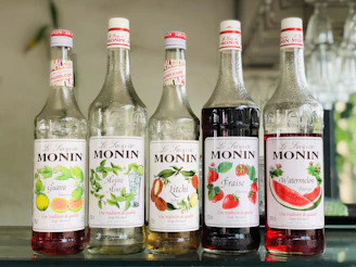 Variety of syrup bottles with vibrant labels lined up against a minimalist white background.