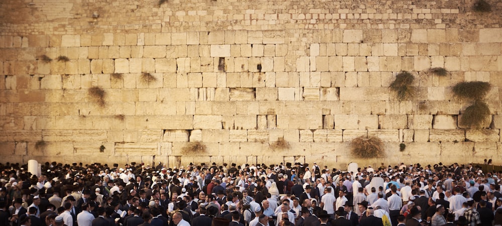 Una multitud de personas de pie frente a un muro de piedra
