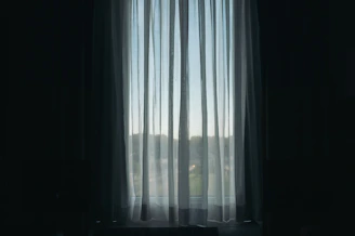 A bright, airy room featuring linen sheer curtains softly flowing by a sunlit window with cordless roller shades partially drawn.