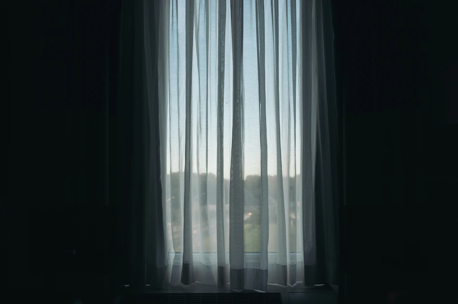 A bright, airy room featuring linen sheer curtains softly flowing by a sunlit window with cordless roller shades partially drawn.