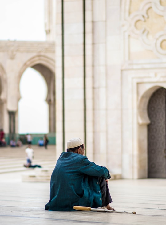 man sitting on concrete pavement during daytime in Hassan II Mosque Morocco