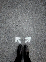 feet on asphalt between two directional arrows