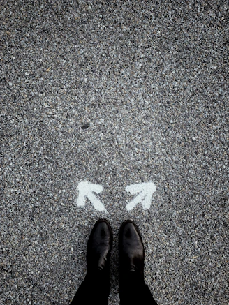 feet on asphalt between two directional arrows