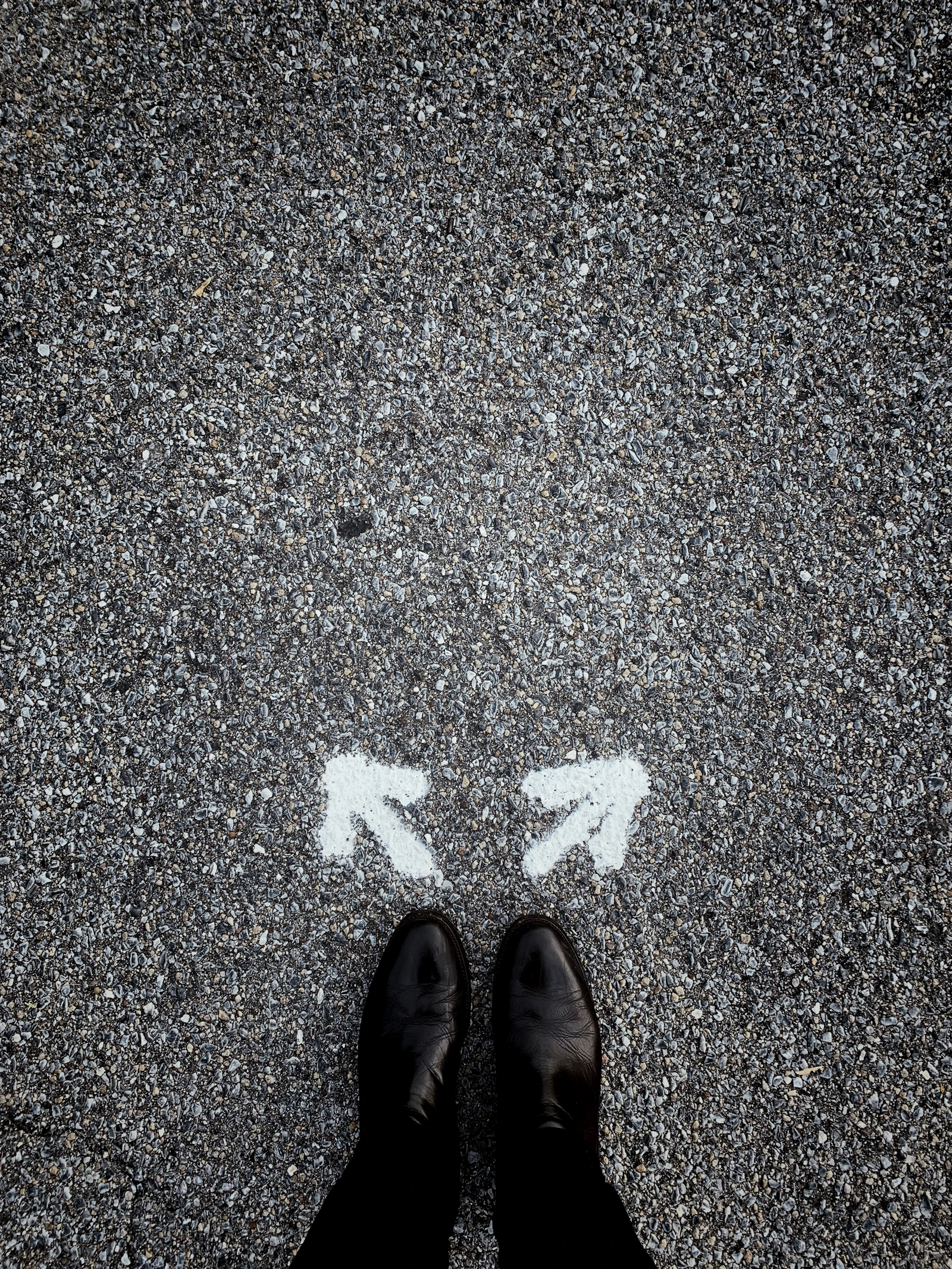 A pair of feet standing on tarmac between two chalk arrows pointing in different directions