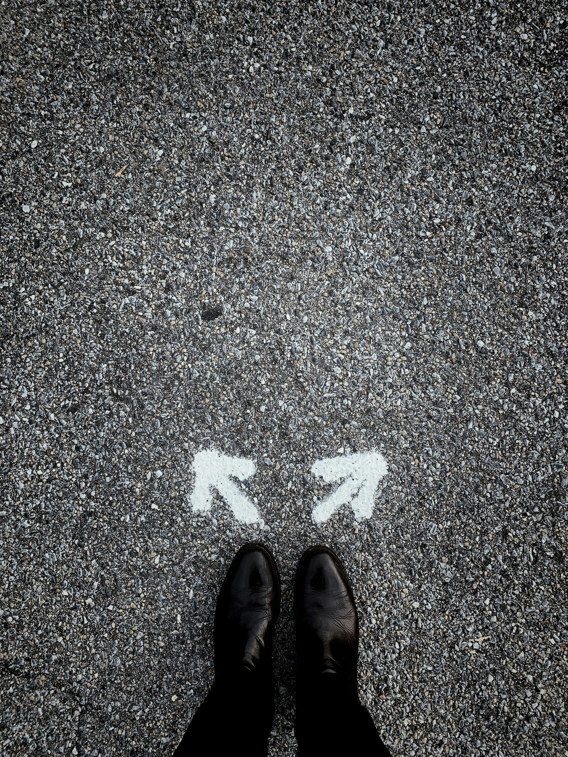 Looking down at a road, there's two arrows on the asphalt showing opposite implied paths.