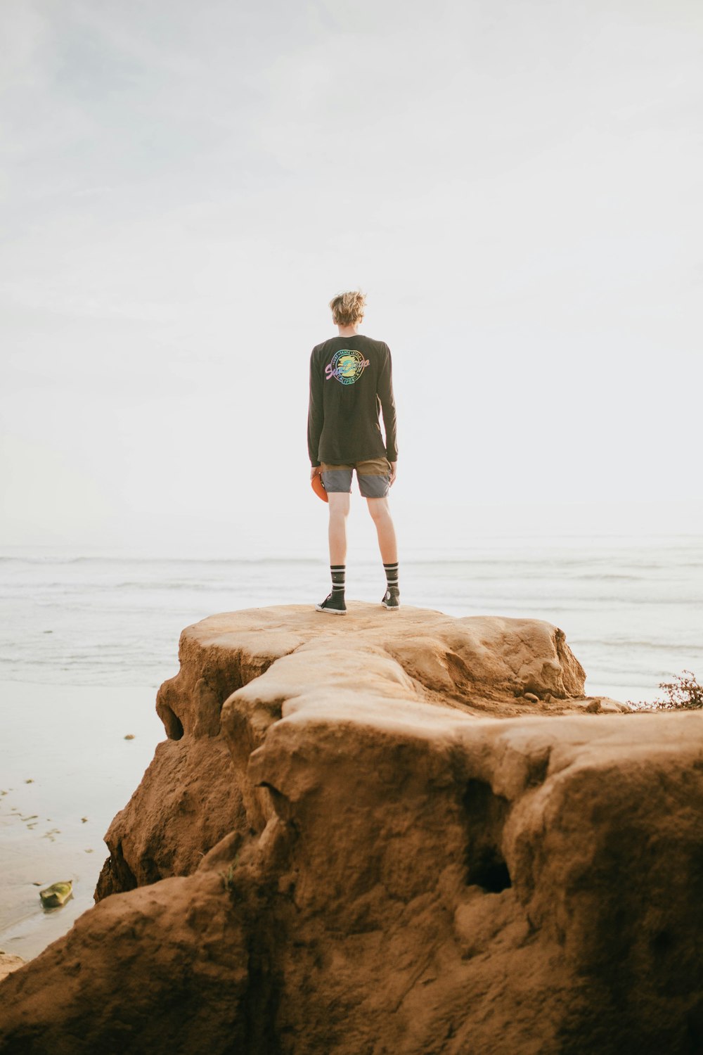 Person, die tagsüber am Rande einer Klippe vor dem Meer steht