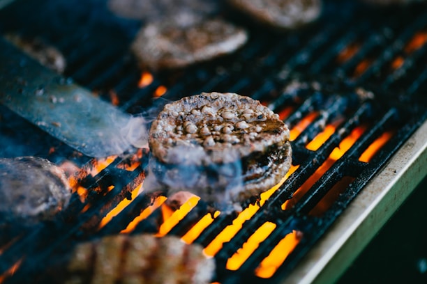 Close-up of a juicy burger sizzling on a flaming grill with smoke rising.
