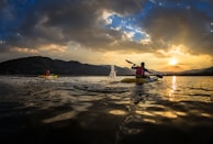 Kayakers paddling on a calm lake at sunset with mountains in the background.