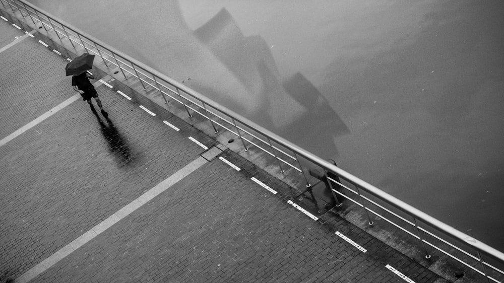 fotografia in scala di grigi di persona che cammina con l'ombrello