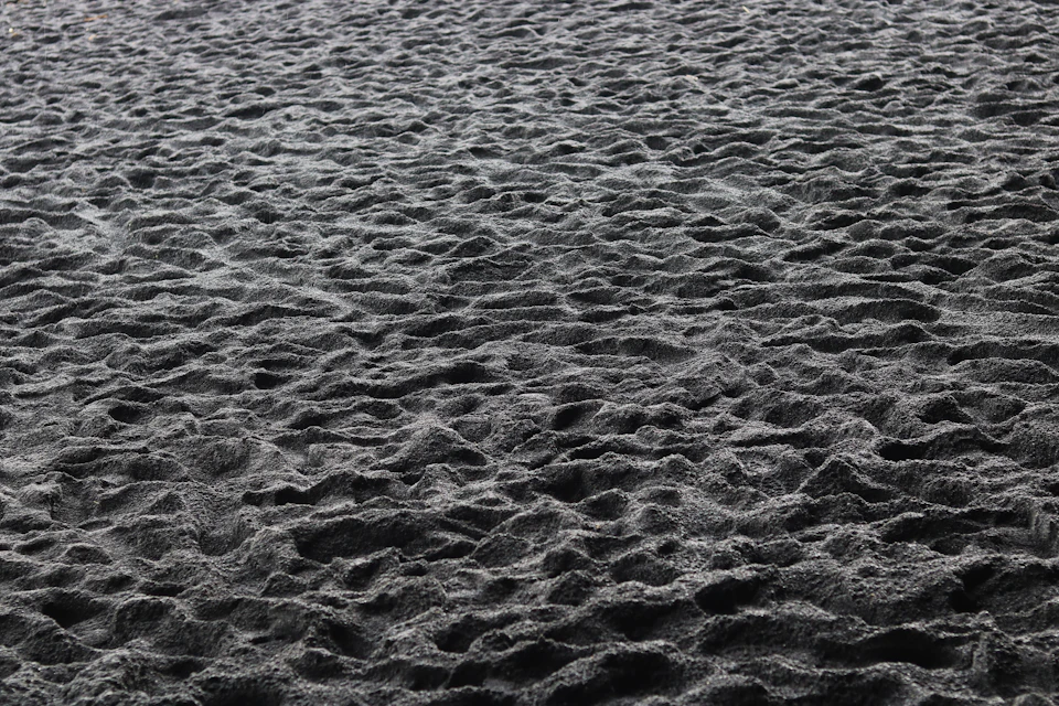 Close-up view of sandy beach with dark gray sand speckled by small white dots