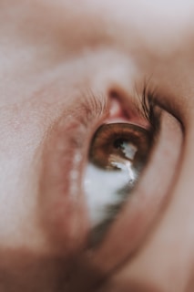 A close-up shot of a human eye with detailed focus on the eyelashes and the smooth surrounding skin texture. The eye reflects some light, adding to the depth and detail of the image.