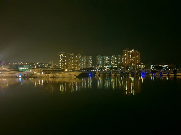 Nighttime cityscape of Dubai Marina glowing behind a moored yacht with ambient lighting.
