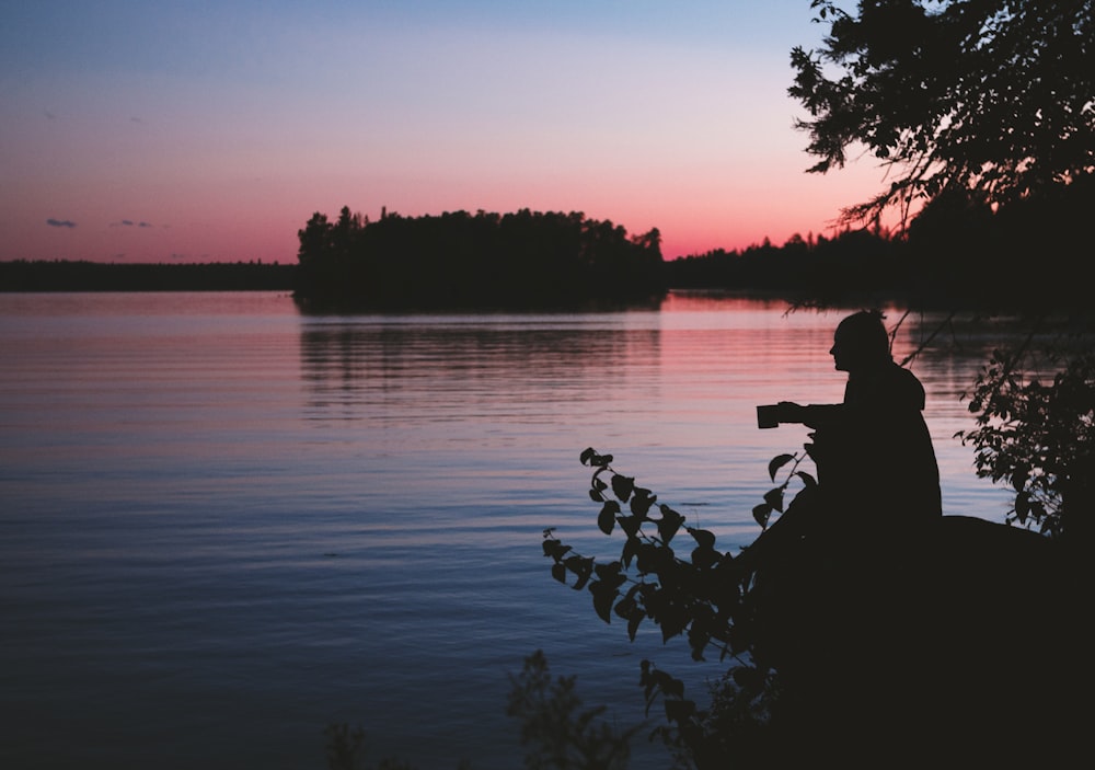 silhouette photo of man sitting beside body of water
