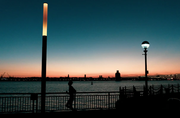Sunset silhouette of a runner crossing a bridge with cityscape background.