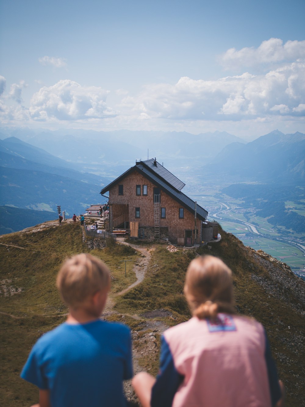 Junge und Mädchen sitzen tagsüber auf einer Klippe mit Blick auf das Haus
