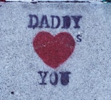 Graffiti on a concrete surface with the words 'Daddy ❤️ You' in black around a red heart shape.