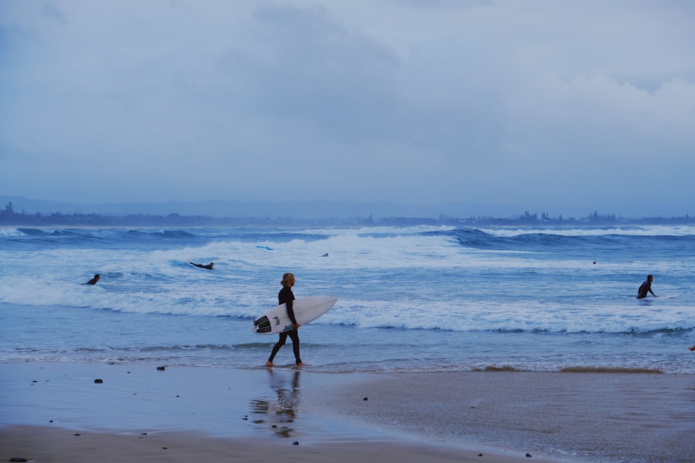 person holding white surfboard on sea shore