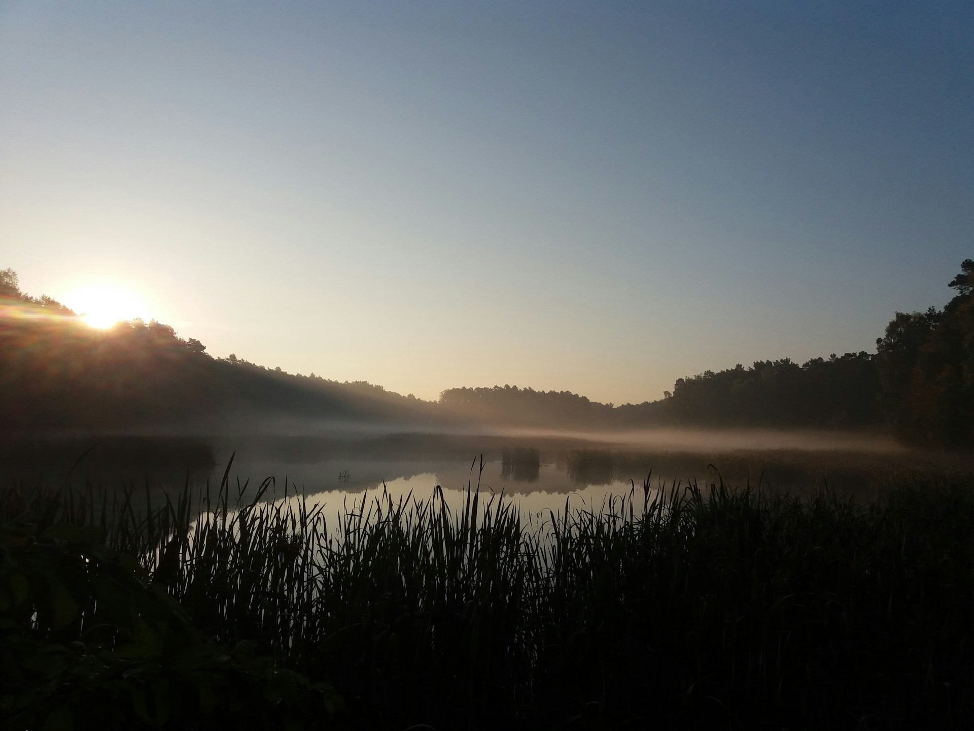 A serene landscape shot of a mountain lake at sunrise with mist hovering over the water.