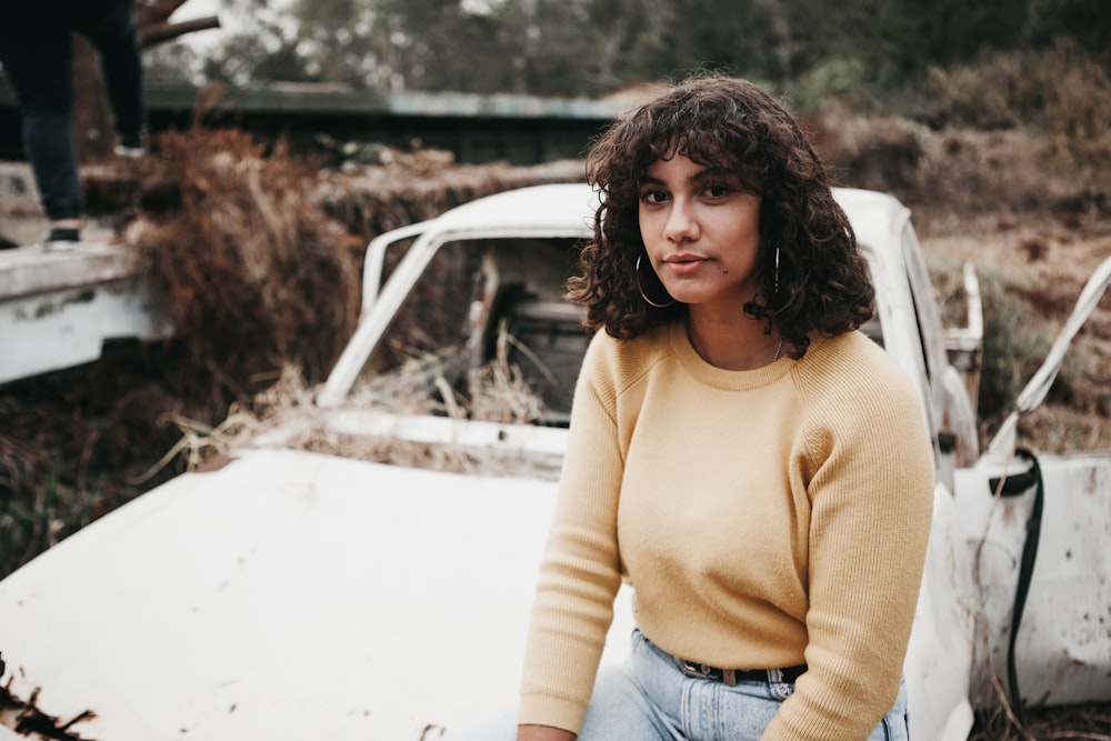 woman wearing yellow sweater sitting on abandoned car