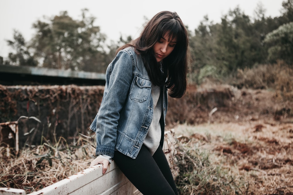 woman wearing blue denim jacket sitting on brown fence