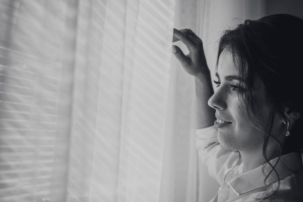 Fotografía en escala de grises de una mujer cerca de una ventana