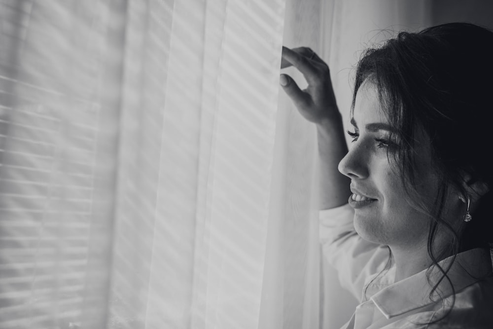 grayscale photography of woman near window